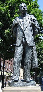 photograph of modern statue of Edwardian male figure with a large moustache in academic gown and wearing badge of the Order of Merit