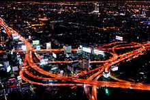 Night photograph looking down at a large elevated road interchange; many billboards along the roads