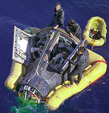 Photo of Armstrong and Scott in the Gemini capsule, in the water. They are being assisted by some recovery crew