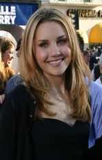 Head shot of a smiling Bynes, a camera and people in the background.